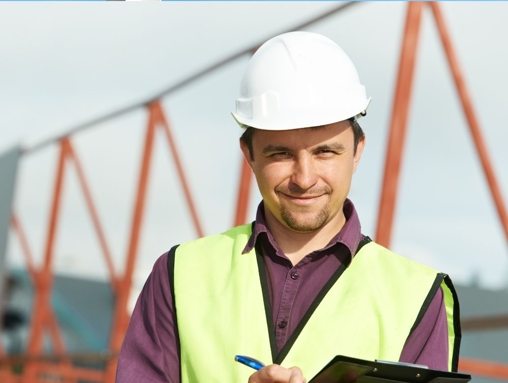 A man smiling in PPE with infrastructure behind him, representing an Artisan 